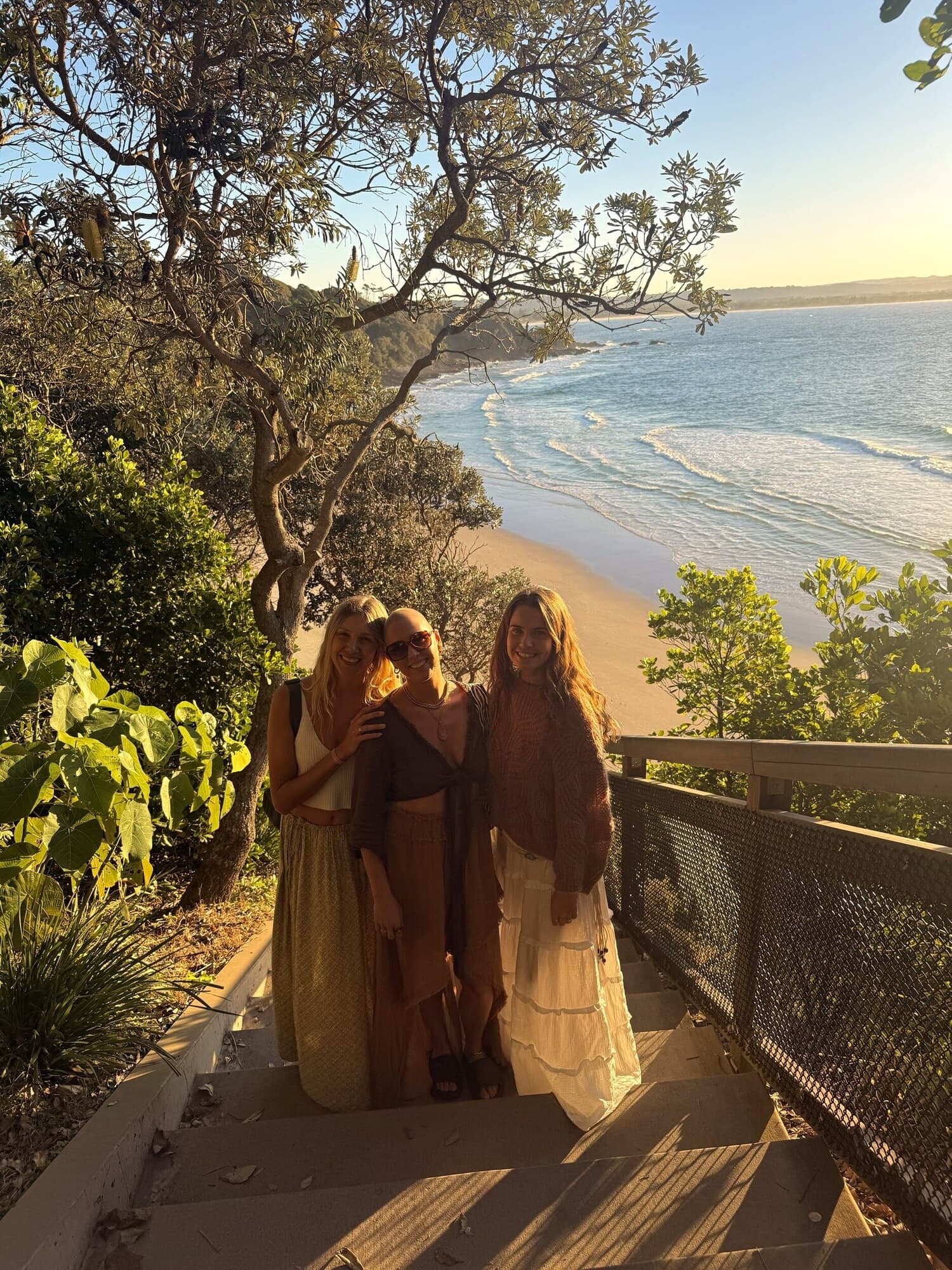 Three tribe members on coastal steps above a beach at golden hour in Australia.