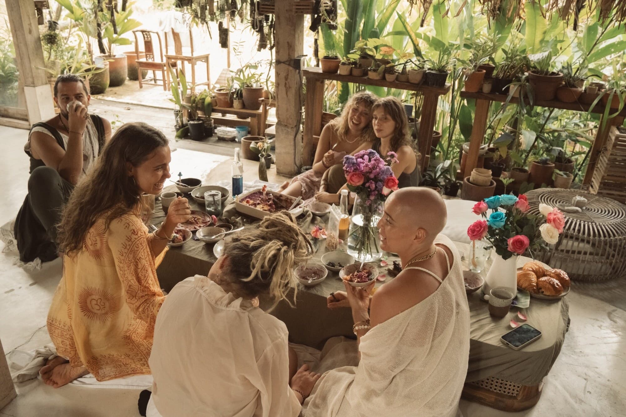Tribe members sharing a low table of flowers and food in an open-air pavilion in Bali.
