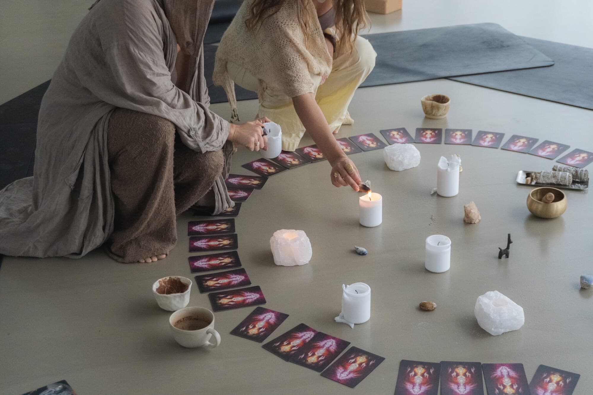 Two tribe members lighting candles around a mandala of cards and crystals in Denmark.
