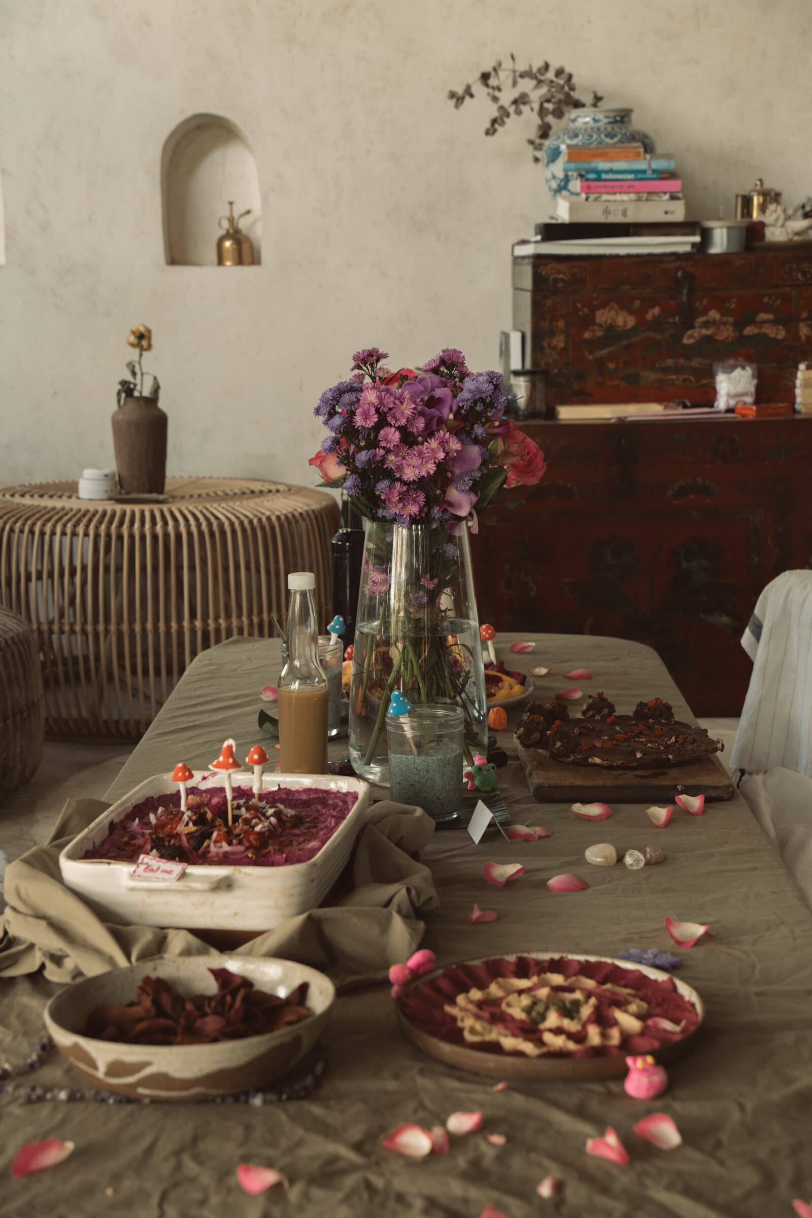 A vase of pink and purple flowers on a gathering table, soft warm light through stone arched windows.
