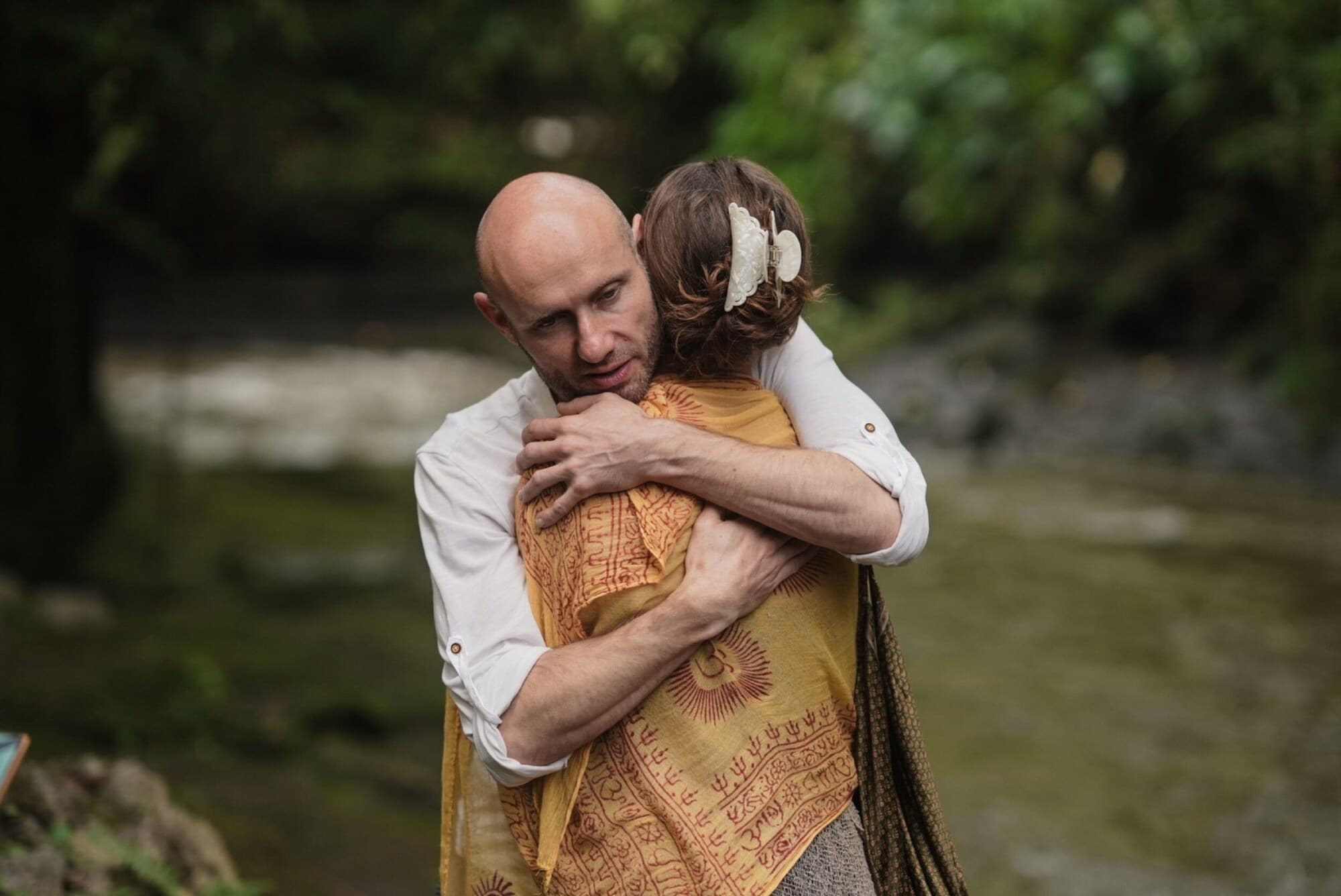 Two tribe members holding each other beside a jungle stream.