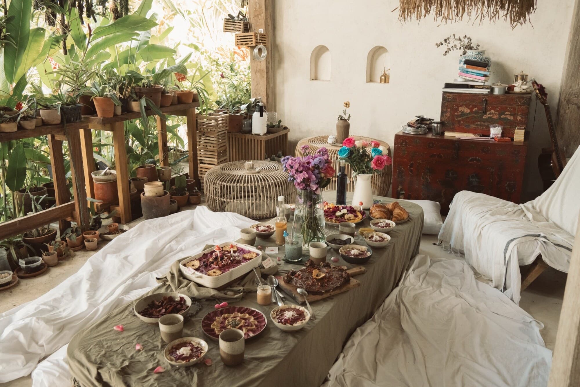 A long shared table in Ubud set with flowers, bowls and cushions, open to the plants outside.